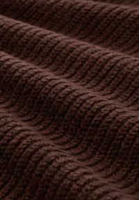 Nahaufnahme von dunkelbraunem gestricktem Stoff mit geripptem Muster und weicher, flauschiger Oberfläche, die wellenförmige Muster erzeugt.