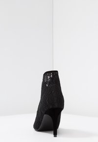 Bottine en dentelle noire au design élégant, avec un talon haut et une texture de tissu douce, mettant en avant un motif floral et un bout lisse et arrondi.