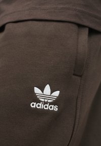 Barna pamut pulóver, fehér Adidas logóval hímzett három levelet ábrázoló mintával és vízszintes csíkokkal az alján.