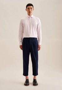 Camicia a righe rosa chiaro con colletto e chiusura con bottoni, abbinata a pantaloni a vita stretta blu navy scuro e scarpe nere. Tessuto dalla texture liscia.
