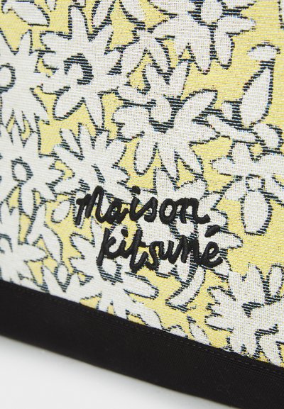 Sac textile floral avec un motif jaune et blanc, un fond noir et un logo brodé "Maison Kitsuné".