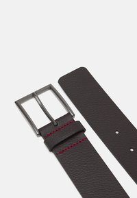 Ceinture en cuir brun foncé avec une finition texturée, dotée d'une boucle métallique et de surpiqûres rouges le long du bord. Se termine par plusieurs trous pour des ajustements.