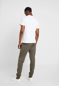 Witte katoenen t-shirt en olijfgroene joggingbroek, beide met een ontspannen pasvorm. Witte sneakers maken de outfit compleet. Geen zichtbare patronen of accenten.
