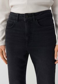 Black denim jeans with a high waist, featuring a button closure, front pockets, and a smooth texture. The fabric is sturdy and stretchy.