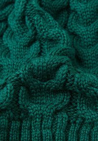 Tessuto lavorato a maglia verde con un intricato motivo a treccia, che mostra texture e morbide pieghe.