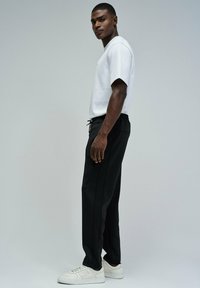 Pantalones de chándal negros con cintura ajustable, combinados con una camiseta blanca de manga corta y zapatillas deportivas blancas. Diseño elegante y ceñido.