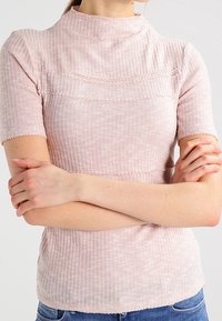 Světle růžový přiléhavý top s krátkými rukávy, žebrovanou texturou, vysokým výstřihem a jemnými horizontálními švy. Hladká a elastická látka.