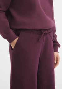 Bordeaux joggingbroek met een elastische tailleband met koord, zijzakken en geribbelde boorden voor een veilige pasvorm. Zacht, gestructureerd materiaal.