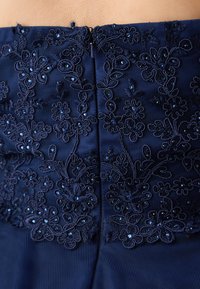 Marineblaues Kleid mit aufwendiger Blumenstickerei und Perlenakzenten, mit einem sicheren Reißverschluss auf der Rückseite und glatter Stoffoberfläche.