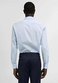 Camicia button-up azzurro chiaro a maniche lunghe, abbinata a pantaloni scuri. Presenta un colletto standard e polsini con bottoni, tessuto dalla texture liscia.