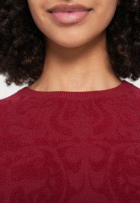 Μπορντό πλεκτό πουλόβερ με υφή, που διαθέτει ριμπ λαιμόκοψη και απαλό φινίρισμα, με διακριτικές λεπτομέρειες σχεδίου σε όλο το κομμάτι.