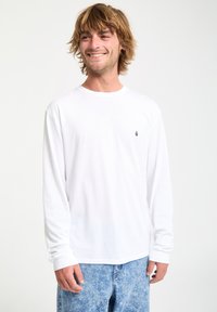 Weißes Langarm-T-Shirt aus Baumwolle. Mit Rundhalsausschnitt, lockerer Passform und kleinem schwarzen Logo auf der linken Brust.