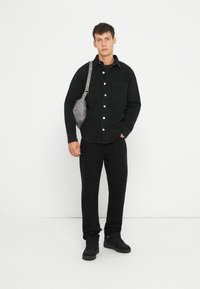 Must jarv denim särk kahe esifrakiga, hall ristiülekande kott, mustad püksid ja mustad tossud, esitatud valge tausta against.
