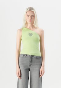 Top verde asimmetrico con spacco sulla spalla, caratterizzato da un design a forma di cuore con strass. Abbinato a jeans grigi a gamba larga.