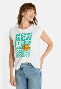Camiseta blanca de algodón con texto ondulado color teal "SEA LINE" y un sol naranja con un patrón de olas azules en la parte inferior; mangas cortas y enrolladas.