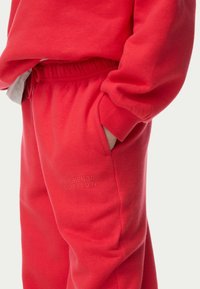 Røde fleece sweatpants med elastisk talje, sidelommer og prægede 'WEEKEND EDITION' tekst på låret. Blød tekstur.