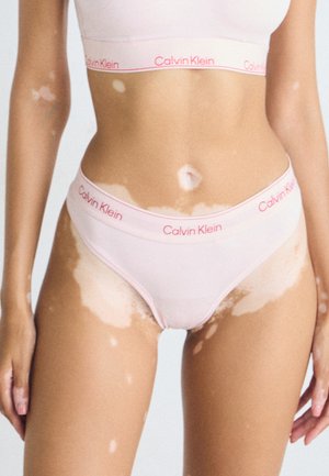 Light pink Calvin Klein bralette and matching briefs feature a smooth texture and elastic bands with white stitching and brand logo accents.