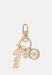 Gold-tone metal keychain with "Guess" branded clasp, circular ring, and four decorative charms including a heart, logo, and script "Ohay".