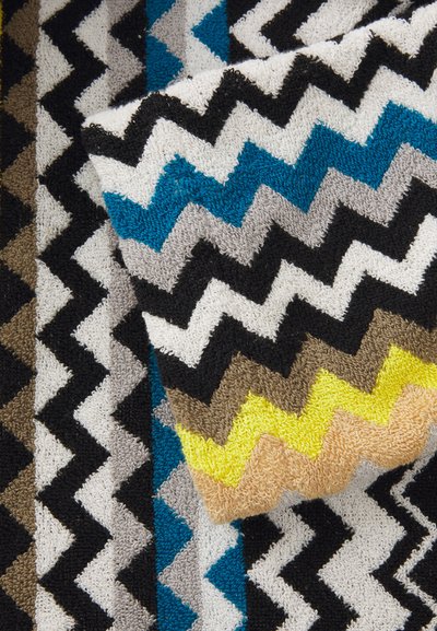 Tessuto con motivo zigzag multicolore in blu, nero, grigio, giallo e beige. Presenta una superficie texturizzata e morbida.