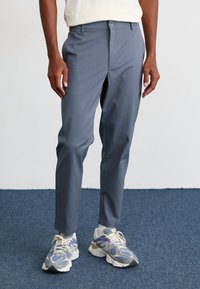 Gray, slim-fit trousers with a smooth texture, featuring a front button closure and side pockets, paired with gray and purple sneakers.