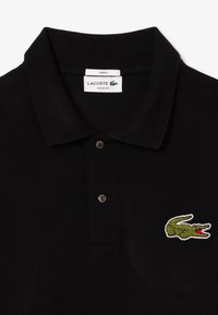 Polo noir en coton texturé avec une patte de boutonnage à trois boutons et un logo crocodile vert brodé sur la poitrine gauche.