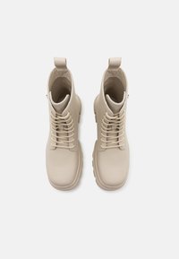 Paire de bottines beige clair à lacets avec languettes de tirage, vue de dessus sur un fond blanc uni.