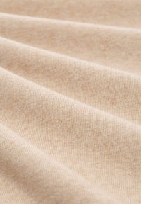 Tela beige claro con una superficie suave y texturizada que presenta un delgado acanalado, dispuesta en suaves pliegues, mostrando su calidad lisa.