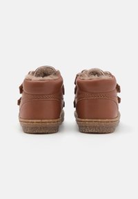 Bottes ankle en cuir marron avec un intérieur doux et doublé de fourrure, des bandes Velcro et des semelles en caoutchouc texturé pour une bonne adhérence.