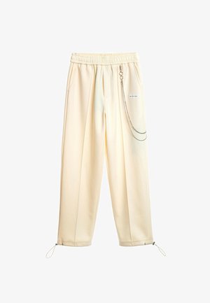 Pantalones color crema con un diseño de pierna ancha, cintura elástica, bolsillos laterales y un detalle de cadena metálica en el lado. Puños ajustables.