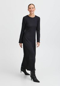 Musta pitkähihainen mekko, jossa on teksturoitu kangas, suora siluetti, puoliväliin säärtä ulottuva pituus, yhdistetty mustiin kärkitossuihin, joissa on korkea korko.
