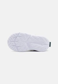 Semelle blanche d'une sneaker avec un motif texturé et un accent vert au niveau du talon. Présente un logo en relief sur le côté.