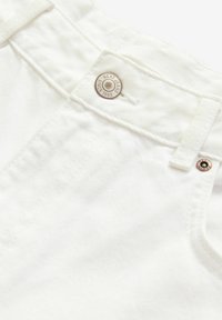 Vita denimjeans med knäppning, texturerat tyg och en märkesbricka av metall. Synliga sömdetaljer längs midjebandet.