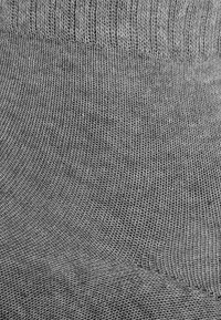 Grauer gestrickter Stoff mit einer glatten Textur, der am oberen Rand über gerippte Details verfügt, wodurch ein allmählich welliges Muster entsteht.