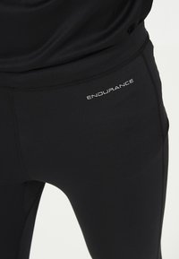 Svarta atletiska leggings med en slät textur, som har en åtsittande design och en liten "ENDURANCE"-logotyp i vitt på vänster lår.