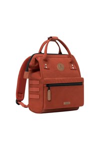 Red canvas backpack with dual handles and a padded strap, featuring a front zipper pocket and logo detail, three side straps, and a durable texture.