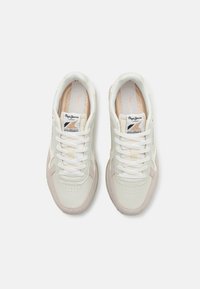 Vita och ljusbeige atletiska skor med texturerat läder, snörning på framsidan, perforerad tå och metalliska accenter på tungan och sidan.