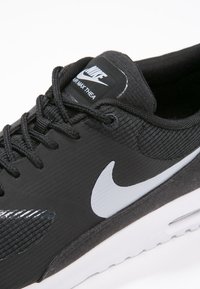Svart Nike Air Max Thea sneaker har en meshöverdel, texturerad yta, vit logotyp och en kontrasterande vit sula. Snörena är svarta.