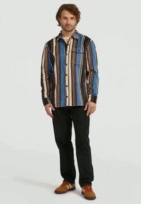 Camisa de flanela multicolorida com riscas verticais em azul, laranja, preto e creme, com um bolso no peito e fecho de botão.