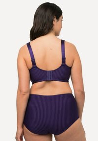 Temně fialová souprava spodního prádla s vertikálními pruhy. Bralette má nastavitelné ramínka a zapínání na háček; spodní část s vysokým pasem a vlnitým lemem.