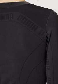 Svart atletisk topp med texturerad tyg, figurnära design och en tonad logotyp längs axelsömmen. Slät finish och kroppsnära siluett.