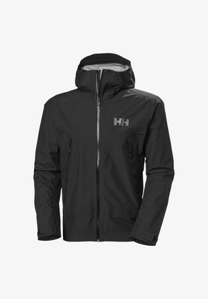 Hand in de zijzak van een zwart jack met gespsluiting aan de mouw en een zwarte heuptas met ritsvakken.