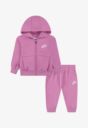 Vaaleanpunainen hupparitakki ja siihen sopivat housut, jotka on valmistettu pehmeästä kankaasta; ominaisuuksiin kuuluu vetoketjukiinnitys ja valkoiset Nike-logo-yksityiskohdat molemmissa osissa.