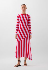 Rood-wit gestreepte jurk met lange mouwen en asymmetrische zoom, geribbelde textuur en getailleerde pasvorm; gecombineerd met zwarte platte sandalen.