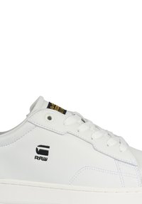 Baskets en cuir blanc avec une texture lisse, dotées d'un logo sur le côté, de lacets et d'une semelle texturée. Couture distincte de couleur contrastante.