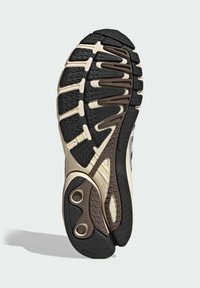 Podešev boty má strukturovaný černý gumový základ, béžovou mezipodešev a výrazný design se drážkami a kruhovými akcenty.