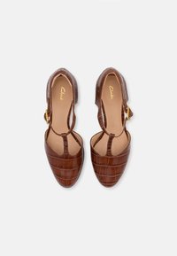 Chaussures en cuir marron avec embossage crocodile, à bout ouvert, avec une bride de cheville et des détails en boucle dorée. Doublure intérieure lisse.