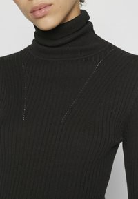 Czarny prążkowany sweter z golfem, o dopasowanej formie, z pionowymi liniami i małymi wycięciami wzdłuż ramion.