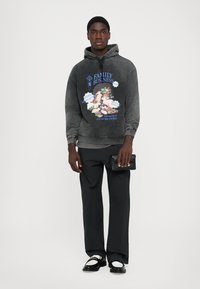 Charcoal gray hoodie with a graphic print featuring colorful illustrations and text. Paired with black, wide-leg pants and shoes.