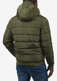 Olive green puffer jacket with a hood, featuring horizontal stitching, ribbed cuffs, and a drawstring closure. Soft, shiny material.