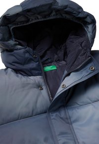 Giacca puffa blu navy con cappuccio; presenta una chiusura zip, bottoni a pressione e fodera interna. Tessuto liscio e resistente con leggera lucentezza.
